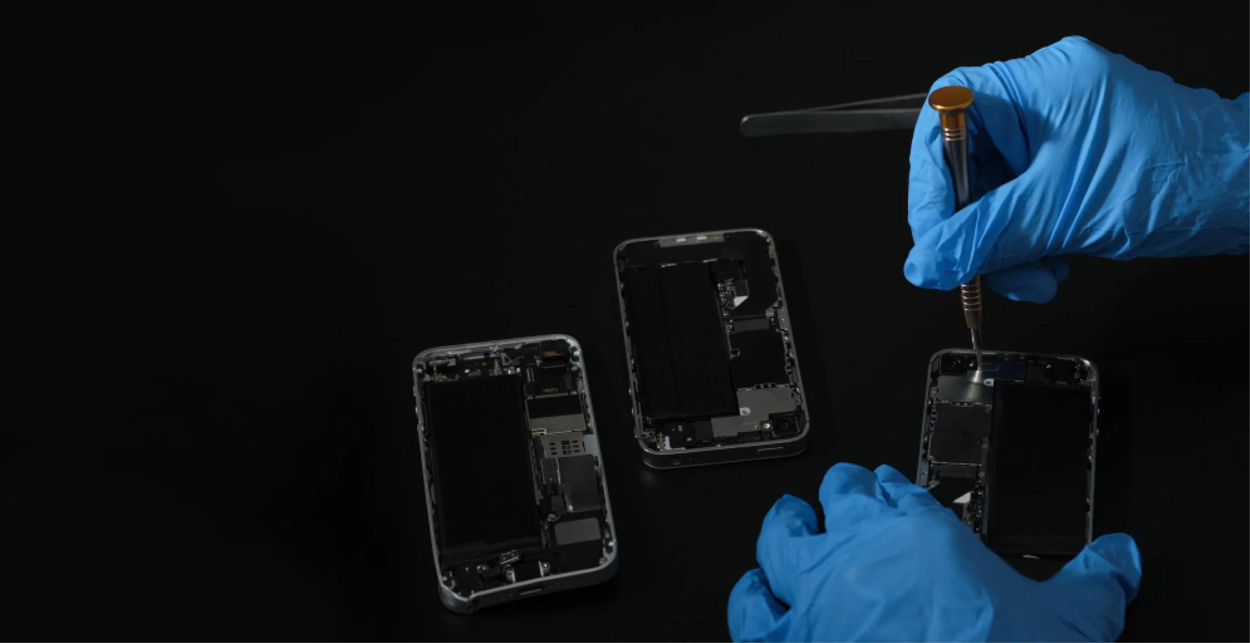 Techniker mit blauen Handschuhen bei der Reparatur von Smartphones auf schwarzem Hintergrund